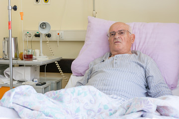 Elderly man laying on a bed in hospital.