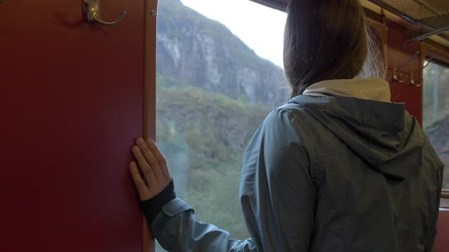 A Woman Standing on a Train Looking out the Window at a Beautiful Mountain Landscape in Norway