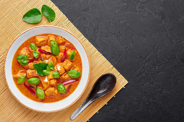 Thai Panang Chicken Curry in white plate at black slate background. Phanaeng Curry is thai cuisine dish with chicken, kaffir lime leaves, red curry sauce and vegetables. Thai food. Copy space