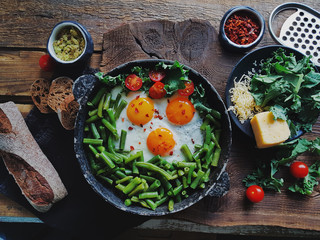 Pan of fresh fried eggs with tomatoes, green beans, bread, spices and herbs on rustic wooden background