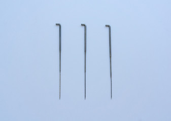 Three steel needles lie parallel to each other on a white background. Concept of felting creative hobby.