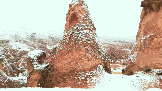 Cinematic aerial view of snowy landscape at Devrent Valley in Cappadocia. Fairy chimneys surronded by snow in Imaginary valley full of unique tuff rock formations in winter season in Cappadocia. 