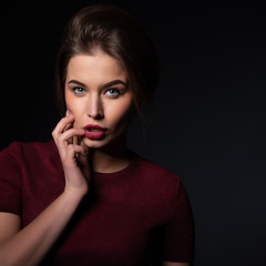 Portrait of attractive young woman over black background. Amazing girl with perfect makeup wearing elegant deep red dress. Beauty and fashion