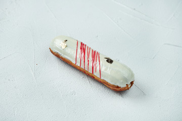 Beautiful and tasty eclair with white-red glaze and vanilla flavor on a white texture background. Close up