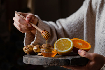 Young woman in holding immunity strengthening kit: ginger, lemon, orange, honey pourring from spoon. Anti virus natural organic treatment. Healthcare, home remedy against cold, influenza. Closeup