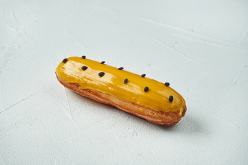 Beautiful and tasty eclair with yellow glaze and mango-passion fruit flavor on a white texture background. Close up