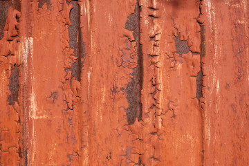 Peeling red paint on a rusty corrugated metal panel