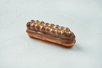 Beautiful and tasty eclair with white-red glaze and salted caramel flavor on a white texture background. Close up