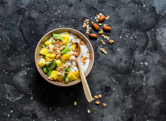 Greek yogurt with tropical fruits and granola on a dark background, top view. Natural yogurt with...