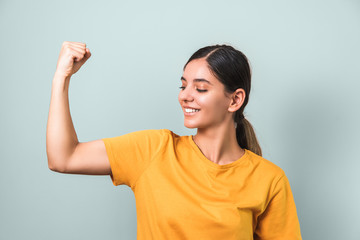 Fototapeta na wymiar women are strong. young attractive brunette in yellow t-shirt showing her biceps against light colored background