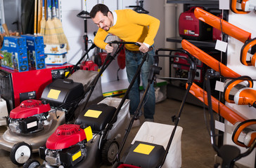 young man deciding on best lawnmower in garden equipment shop