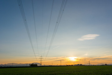 Power transimission lines running across fields at sunset.