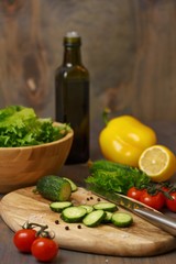 The process of preparing a fresh green salad of cucumber, cherry tomato, bell pepper, green lettuce with lemon and olive oil