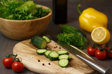 The process of preparing a fresh green salad of cucumber, cherry tomato, bell pepper, green lettuce with lemon and olive oil