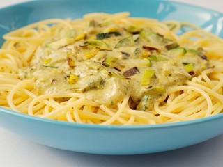 Spaghetti with a cream sauce with zucchini and leek in a light blue plate on a white background from above.