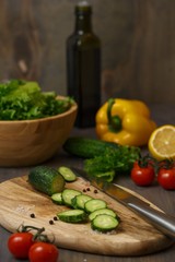 The process of preparing a fresh green salad of cucumber, cherry tomato, bell pepper, green lettuce with lemon and olive oil