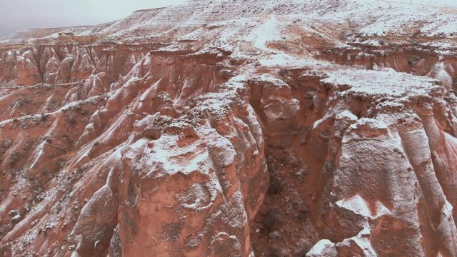 Cinematic aerial view of snowy landscape at Devrent Valley in Cappadocia. Fairy chimneys surronded by snow in Imaginary valley full of unique tuff rock formations in winter season in Cappadocia. 