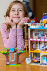 Little girl plays with a children's constructor at home. Little girl playing with lots of colorful plastic blocks constructor and builds house. vertical photo