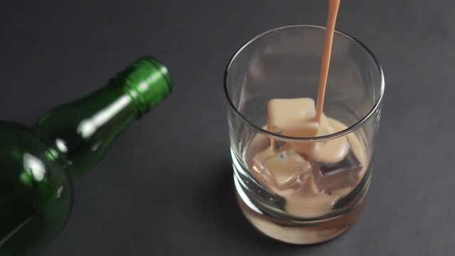 Irish cream liqueur is poured into a glass with ice cubes. Empty green bottle. Alcoholic drinks at the bar.