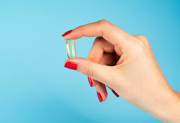 Woman hand holding single yellow Cod Liver Oil capsule on blue background