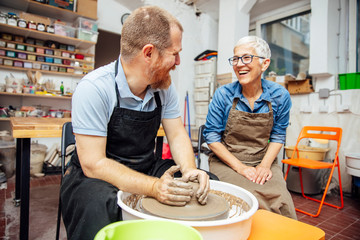 Senior woman spinning clay on a wheel with teacher at pottery class