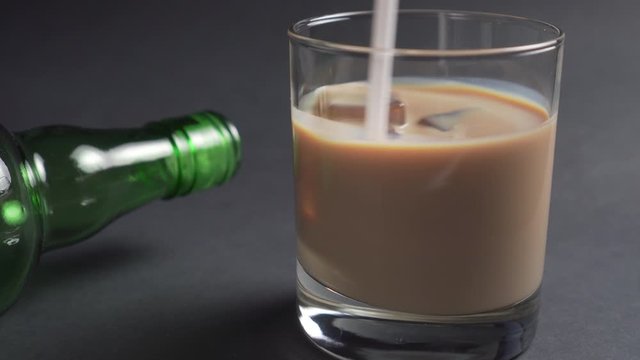 drinking tub stirs Irish cream liqueur with ice cubes in a glass. Empty green alcohol bottle. Close-up