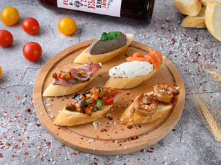 Assorted bruschetta with various toppings on a round wooden board