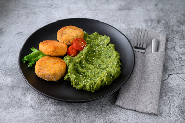 Mashed potatoes with broccoli and fish cakes on a black plate