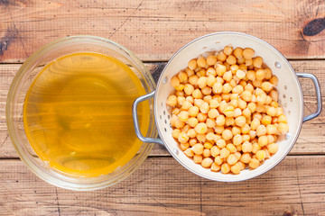 Boiled chickpeas in a colander and water from chickpea aquafab on a wooden table, top view, selective focus