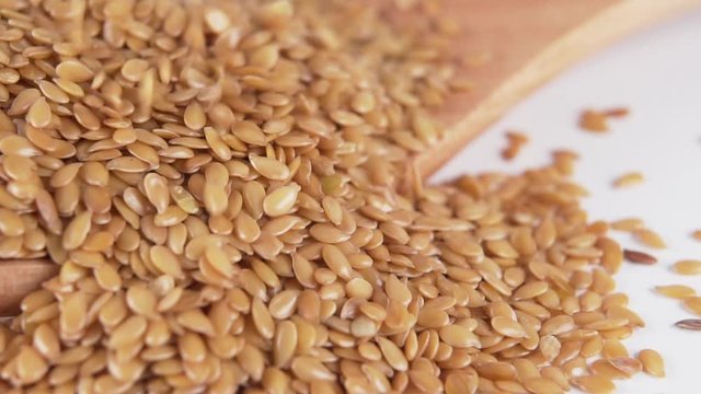 flax seeds fall in a heap on a wooden spoon on a white kitchen table close-up. Macro shot. Slow motion.
