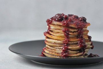 Pancakes with berry jam on a black plate. Close-up. Light background. In the background is a cup of jam. Free space for text.