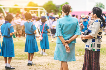 Obraz premium Asian female teacher stand to control the students playing music while lining up to pay respect to the national flag in the morning in school.