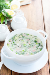 Traditional summer okroshka soup with sausage and vegetables in a white bowl, copy space