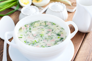 Traditional summer okroshka soup with sausage in a white bowl, selective focus