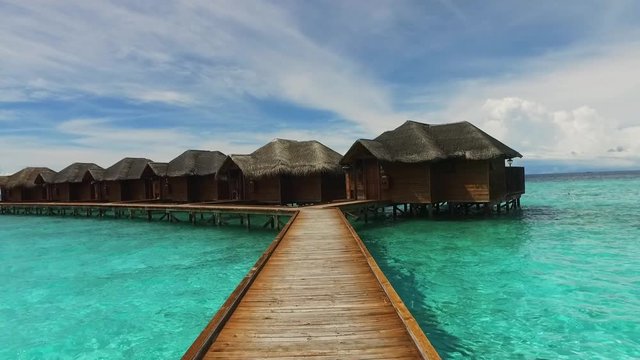 Maldive island bungalow on water. Walking on wooden bridge to luxury hotel. Maldives travel destination. Blue lagoon. Cottage in Indian ocean. Relaxation and romantic place. Resort villa in paradise.
