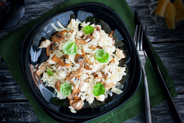 Traditional Italian risotto with chicken and mushrooms on a black plate, selective focus, top view