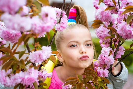 Lovely teenager girl with pink cherry sakura flowers in pink dress at beautiful garden. Cherry blossom. Funny face.