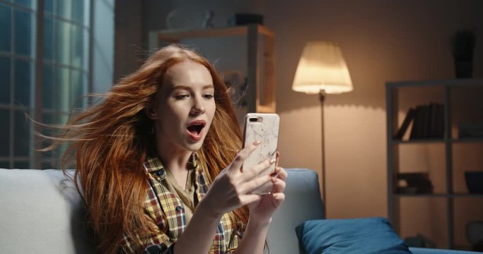 Astonished redhead caucasian girl looking at smartphone, wind blowing hair, Model reading breaking news, getting an amazing discount during online shopping or shocked by event 4k footage