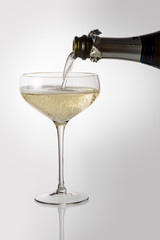 Bottle pouring sparkling wine into champagne cup glass