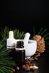 natural production concept, pine cone with nuts, glass bottle and mortar on a black background