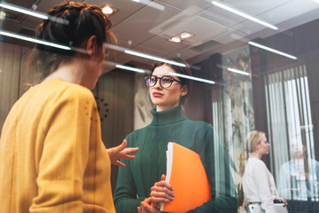 Two young positive businesswoman meeting in openspace office. Female coworker conversation indoor...