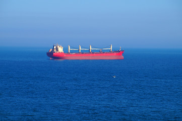 red cargo ship at sea on the horizon