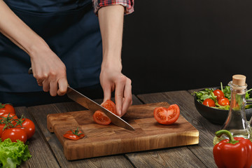 Woman cooking fresh healthy salad. Female hands cutting vegetables on board on wooden table with copyspace.