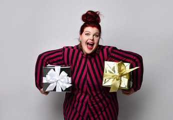 Obese lady in striped dress and earrings. Holding golden and silver gift boxes, overjoyed, posing on white photo background