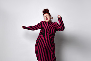 Obese redhead lady in striped dress and earrings. She reaching her hand to you while posing...