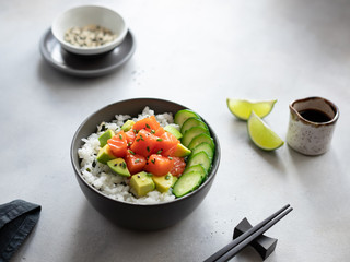 salmon poke bowl with rice, avocado, cucumber and soy sauce on a gray concrete background. traditional Hawaiian raw fish salad. horizontal image. place for text.