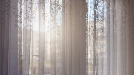 delicate white curtain with nice floral patterns hangs against bright sunlight
