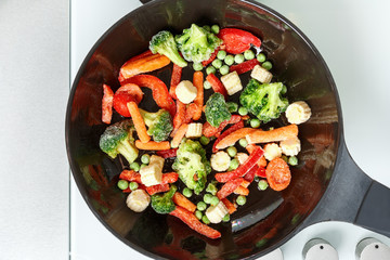 Frying frozen mix vegetables in a pan. Prefabricated top view close-up