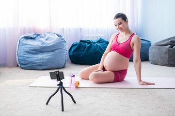 Online lessons for pregnant women. European woman shoots a video fitness lesson on the phone. Waiting for a miracle. Yoga for expectant mothers.
