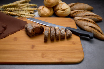 Delicious breads next to ears of wheat on a wooden board.